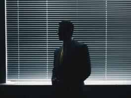 Diversité, égalité, inclusion ? Pas chez UBS Un homme en costard-cravate est debout devant une fenêtre, la pièce est assombrie.