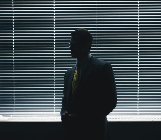 Diversité, égalité, inclusion ? Pas chez UBS Un homme en costard-cravate est debout devant une fenêtre, la pièce est assombrie.