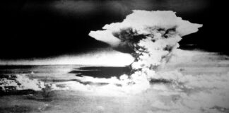 Photographie en noir et blanc prise depuis les airs : un vaste nuage en forme de champignon s’élève au-dessus de Hiroshima.