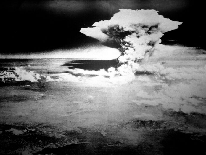 Photographie en noir et blanc prise depuis les airs : un vaste nuage en forme de champignon s’élève au-dessus de Hiroshima.