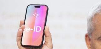 Un homme tient un smartphone sur lequel apparaît en grand le mot ‹e-ID›. L’image illustre l’identité électronique prévue en Suisse