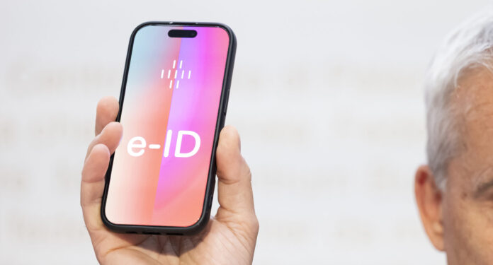 Un homme tient un smartphone sur lequel apparaît en grand le mot ‹e-ID›. L’image illustre l’identité électronique prévue en Suisse