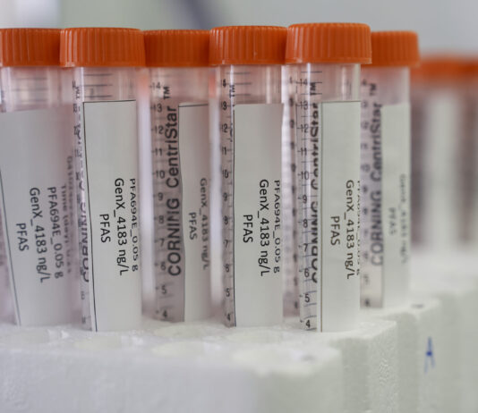 PFAS : le Parlement ne prend que des mesures limitées contre ces substances chimiques persistantes Vue rapprochée de plusieurs tubes à centrifuger Corning CentriStar, munis de bouchons orange et d’étiquettes indiquant « PFA694E 0,05 g – GenX 4183 ng/L – PFAS », rangés dans un support en mousse blanche.