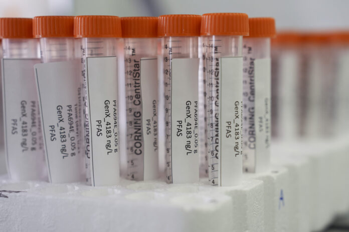 PFAS DRINKING WATER Vue rapprochée de plusieurs tubes à centrifuger Corning CentriStar, munis de bouchons orange et d’étiquettes indiquant « PFA694E 0,05 g – GenX 4183 ng/L – PFAS », rangés dans un support en mousse blanche.