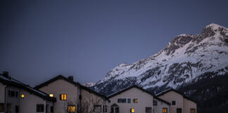 Vue de nuit tombante d’un petit ensemble de maisons beiges aux toits foncés à Sils, aux Grisons, dont plusieurs fenêtres sont baignées d’une lumière chaude. Elles se dressent au-dessus d’un champ enneigé, devant le flanc d’une haute montagne également couverte de neige, sous un ciel bleu sombre de crépuscule. Le canton des Grisons met en garde contre des hausses d'impôts entraînée par la suppression de la valeur locative.