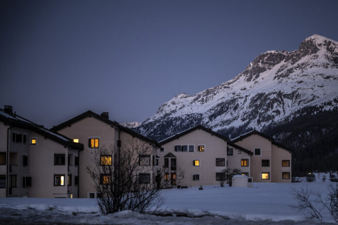 Vue de nuit tombante d’un petit ensemble de maisons beiges aux toits foncés à Sils, aux Grisons, dont plusieurs fenêtres sont baignées d’une lumière chaude. Elles se dressent au-dessus d’un champ enneigé, devant le flanc d’une haute montagne également couverte de neige, sous un ciel bleu sombre de crépuscule. Le canton des Grisons met en garde contre des hausses d'impôts entraînée par la suppression de la valeur locative.