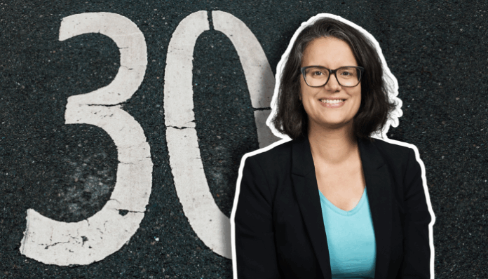 Montage montrant en arrière-plan le chiffre 30 peint en blanc sur une chaussée asphaltée, et au premier plan sur la droite, le buste d’une femme souriante aux cheveux mi-longs, portant des lunettes, un blazer noir et un t-shirt turquoise, avec un léger trait de contour blanc tout autour d’elle.