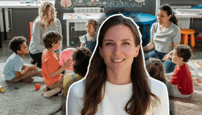 Au premier plan, une jeune femme aux cheveux bruns et longs, souriante, vêtue d’un pull blanc, sur un fond clair. En arrière-plan, une salle où sept enfants sont assis en cercle sur un grand tapis gris : certains tiennent des ballons ou des jouets. Deux enseignantes, l’une aux cheveux blonds assise à gauche, l’autre aux cheveux foncés assise à droite, encadrent le groupe et les regardent attentivement. Des tables basses et du matériel pédagogique décorent la pièce.