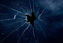 Féminicides : la réalité qui heurte Photo en gros plan d’une vitre sombre brisée, avec des fissures en éventail rayonnant à partir d’un trou central.