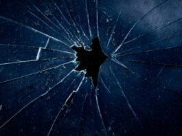 Féminicides : la réalité qui heurte Photo en gros plan d’une vitre sombre brisée, avec des fissures en éventail rayonnant à partir d’un trou central.