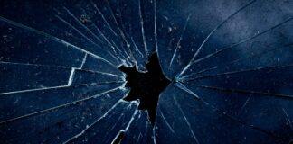Féminicides : la réalité qui heurte Photo en gros plan d’une vitre sombre brisée, avec des fissures en éventail rayonnant à partir d’un trou central.