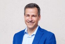 Les ONG sont sous pression : « Notre travail renforce la démocratie » Portrait d’un homme d’âge moyen, cheveux courts poivre et sel, souriant, vêtu d’une veste bleu vif et d’une chemise bleu clair. Il se tient debout, les mains dans les poches, devant un mur uni de couleur claire