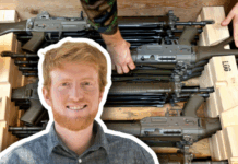 Loi sur le matériel de guerre : « Plus il y a d’armes en circulation, plus le danger pour les civils augmente » Portrait détouré en médaillon d’un homme roux souriant, chemise à carreaux, superposé sur l’image d’arrière-plan montrant plusieurs fusils d’assaut empilés dans des caisses en bois, deux mains en uniforme les ajustant.