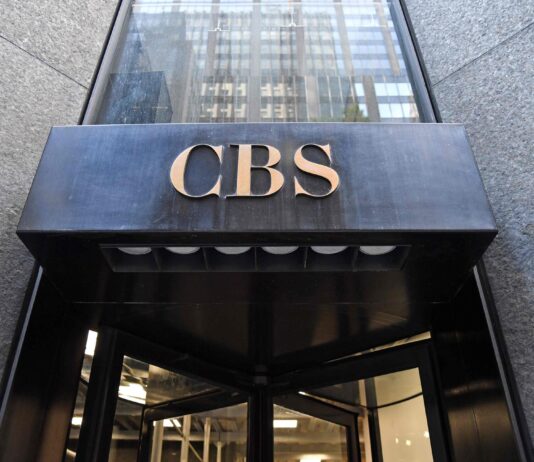 Comment des milliardaires ont transformé une chaîne de télévision américaine traditionnelle en une machine de propagande Entrée d’un immeuble : au-dessus d’une porte tournante en verre, un auvent en métal noir supporte en son centre le sigle « CBS » en lettres dorées. La façade autour est en pierre grise.