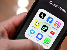 Initiative anti-SSR : plus de fausses nouvelles, moins de vérification Gros plan sur une main tenant un smartphone : à l’écran, un dossier nommé « Social Media » affiche neuf icônes d’applications disposées en grille : X (anciennement Twitter), Facebook, Instagram, Snapchat, TikTok, YouTube, Telegram, Signal et WhatsApp. L’arrière-plan est flou, mettant l’accent sur l’écran du téléphone.
