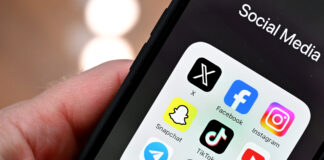 Initiative anti-SSR : plus de fausses nouvelles, moins de vérification Gros plan sur une main tenant un smartphone : à l’écran, un dossier nommé « Social Media » affiche neuf icônes d’applications disposées en grille : X (anciennement Twitter), Facebook, Instagram, Snapchat, TikTok, YouTube, Telegram, Signal et WhatsApp. L’arrière-plan est flou, mettant l’accent sur l’écran du téléphone.