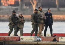 Venezuela : Trump mise illégalement sur « le droit du plus fort » « Sur un quai en bord d’eau, quatre agents en tenue tactique — dont certains portent des blousons marqués “DEA” — escortent Nicolàs Maduro et Cilia Flores menottées vêtues de blousons et pantalons beiges. Le soleil couchant teinte le ciel d’orangé, et des blocs de béton peints en rouge et blanc délimitent le quai devant une surface d’eau calme. »