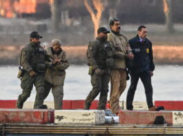 Venezuela : Trump mise illégalement sur « le droit du plus fort » « Sur un quai en bord d’eau, quatre agents en tenue tactique — dont certains portent des blousons marqués “DEA” — escortent Nicolàs Maduro et Cilia Flores menottées vêtues de blousons et pantalons beiges. Le soleil couchant teinte le ciel d’orangé, et des blocs de béton peints en rouge et blanc délimitent le quai devant une surface d’eau calme. »