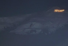 Bonnes nouvelles en janvier : résistance à Davos, le stalking est un délit et l’Espagne introduit un AG à 60 euros Vue nocturne d’un versant montagneux sombre sous un ciel étoilé. Sur une crête à droite, un message lumineux en lettres incandescentes affiche « NO KINGS », se détachant nettement sur le relief obscur.