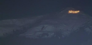 Bonnes nouvelles en janvier : résistance à Davos, le stalking est un délit et l’Espagne introduit un AG à 60 euros Vue nocturne d’un versant montagneux sombre sous un ciel étoilé. Sur une crête à droite, un message lumineux en lettres incandescentes affiche « NO KINGS », se détachant nettement sur le relief obscur.