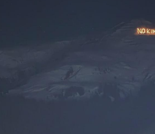 Bonnes nouvelles en janvier : résistance à Davos, le stalking est un délit et l’Espagne introduit un AG à 60 euros Vue nocturne d’un versant montagneux sombre sous un ciel étoilé. Sur une crête à droite, un message lumineux en lettres incandescentes affiche « NO KINGS », se détachant nettement sur le relief obscur.