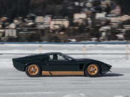 La richesse disproportionnée menace la démocratie vue de profil d’une voiture de sport classique à moteur central, de teinte vert foncé, jantes dorées, filant à vive allure sur une surface gelée et enneigée. À l’arrière-plan, un village aux façades pastel apparaît flou, soulignant l’effet de vitesse.