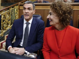 Contre-courant humain : l’Espagne veut régulariser un demi-million de migrant-es Espagne : deux personnes assises côte à côte dans un hémicycle aux boiseries et rambardes dorées. À gauche, Pedro Sánchez, Premier ministre espagnol, un homme en costume bleu foncé, chemise blanche et cravate grise, semble prendre la parole. À droite, sa première vice-première ministre, Maria Jesus Montero, une femme portant un tailleur rouge sourit en le regardant.