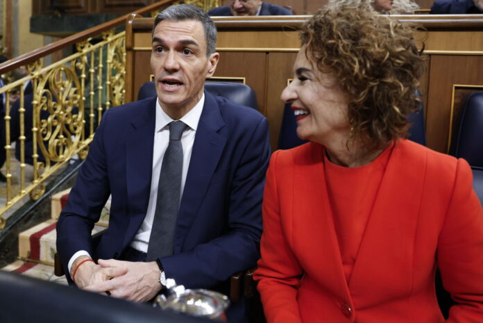 Spanish PM Sanchez attends a plenary session of the lower house of parliament Espagne : deux personnes assises côte à côte dans un hémicycle aux boiseries et rambardes dorées. À gauche, Pedro Sánchez, Premier ministre espagnol, un homme en costume bleu foncé, chemise blanche et cravate grise, semble prendre la parole. À droite, sa première vice-première ministre, Maria Jesus Montero, une femme portant un tailleur rouge sourit en le regardant.