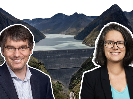 Le fonds climat, késako ? Réponses de Roger Nordmann Cette image montre deux portraits circulaires superposés devant une vue panoramique d’un barrage et d’un lac de montagne. À gauche, Roger Nordmann, un homme souriant porte une veste sombre et une chemise claire. À droite, Oriane Sarrasin, une femme souriante, vêtue d’une veste noire et d’un haut bleu, porte des lunettes. En arrière-plan, on distingue un grand barrage en béton ainsi qu’un lac entouré de montagnes escarpées, sous un ciel dégagé.