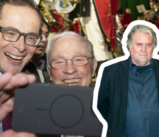 Steve Bannon, stratège politique de Donald Trump — et de l’UDC Christoph Blocher et Roger Köppel (UDC), deux hommes d’âge mûr, vêtus de costumes sombres et portant des lunettes, se penchent l’un vers l’autre en souriant pour un selfie : l’un tient un smartphone devant eux. En arrière-plan, un groupe fanfare en uniforme rouge et blanc joue des cuivres sur scène. Sur la droite de l’image, se détache en surimpression le buste de Steve Bannon, un homme d’une cinquantaine d’années, en chemise et veste décontractées, les mains dans les poches, bordé d’un liseré blanc.