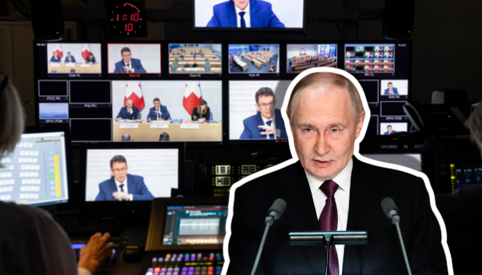 Une régie de production vidéo en éclairage tamisé, avec au premier plan un pupitre de mixage multimédia et plusieurs écrans de contrôle affichant des plans d’une conférence de presse du Conseil fédéral sur l'initiative anti-SSR (tables, orateurs et drapeaux suisses). En surimpression, Vladimir Poutine, un homme en costume sombre et cravate, debout derrière un pupitre équipé de deux micros, semble s’adresser à un auditoire.