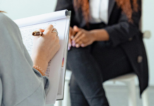 300 000 francs : la Commission des finances vote contre une meilleure aide aux victimes Personne de dos tenant un stylo et un bloc-notes, écrivant des notes manuscrites, en face d’une autre personne assise sur un tabouret, les mains jointes sur les genoux, vêtue d’un tailleur sombre.