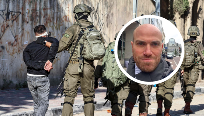 À l'arrière-plan, des militaires israéliens équipés de gilets tactiques et d'armes encadrent une personne en veste noire, mains attachées dans le dos, face à un mur couvert de graffitis. En superposition, un médaillon circulaire présente le portrait d'un homme d'âge moyen, chauve, avec une barbe courte, photographié dans un environnement urbain.