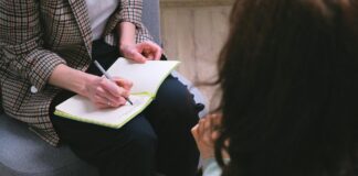 300 000 francs pour l’aide aux victimes : le Parlement corrige une décision désastreuse Une professionnelle portant une veste à carreaux prend des notes avec un stylo dans un carnet ouvert posé sur ses genoux, assise face à une personne aux cheveux bruns vue de dos, dans ce qui semble être un entretien ou une séance de consultation.