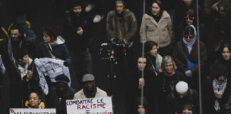 Les agressions racistes continuent d’augmenter L'image montre un groupe de personnes participant à une manifestation à Lausanne après la mort de Marvin. Plusieurs individus tiennent des pancartes avec des messages contre le racisme et la violence policière. Les pancartes portent des inscriptions telles que "Combattre le racisme - Dévoiler un système sans compromis" et "Ma peau n'est pas un costume, ma peau n'est pas une menace #StopBlackFace #StopPoliceViolence". Les manifestants sont vêtus chaudement, suggérant que l'événement a lieu en hiver. L'atmosphère semble sérieuse et déterminée, avec des participants de divers âges et origines ethniques.