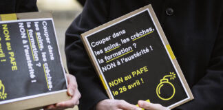 LAFE : Fribourg a un problème de recettes, pas de dépenses Deux personnes vêtues de manteaux sombres tiennent des pancartes artisanales à fond noir avec du texte en blanc et jaune. On peut lire sur la pancarte principale : « Couper dans les soins, les crèches, la formation ? NON à l'austérité ! NON au PAFE le 26 avril ! », accompagnée d'un pictogramme de bombe en jaune. La seconde pancarte, partiellement visible, affiche un message similaire.