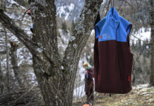 Affaiblissement du service civil : une attaque frontale de la droite Un gilet du Service civil suisse (bicolore bleu et bordeaux) accroché à un arbre en forêt, avec en arrière-plan une personne travaillant dans un paysage hivernal de montagne.