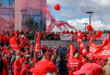 Bonnes nouvelles en mai : la grève reconnue comme droit fondamental, la Belgique résiste à l’austérité et l’ONU adopte une résolution pour le climat Photo montrant une large foule de manifestants lors d'une action syndicale. Les participants, majoritairement vêtus de vestes rouges, brandissent des drapeaux et banderoles aux couleurs des syndicats CGSP, FGTB et CSC. Des ballons rouges flottent dans les airs tandis que des fumigènes rouges sont allumés en arrière-plan. On peut lire sur les banderoles des slogans tels que « Je suis statut », « Touche pas à ma fonction » et « Services publics de qualité », indiquant une mobilisation en défense du secteur public.