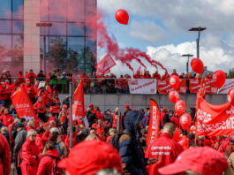 Bonnes nouvelles en mai : la grève reconnue comme droit fondamental, la Belgique résiste à l’austérité et l’ONU adopte une résolution pour le climat Photo montrant une large foule de manifestants lors d'une action syndicale. Les participants, majoritairement vêtus de vestes rouges, brandissent des drapeaux et banderoles aux couleurs des syndicats CGSP, FGTB et CSC. Des ballons rouges flottent dans les airs tandis que des fumigènes rouges sont allumés en arrière-plan. On peut lire sur les banderoles des slogans tels que « Je suis statut », « Touche pas à ma fonction » et « Services publics de qualité », indiquant une mobilisation en défense du secteur public.