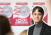 Salaire minimum : « La droite patronale en SManque d’argument » Une personne portant un blazer noir et un col roulé gris se tient devant des affiches de campagne électorale. Les affiches, sur fond rose et blanc, présentent des pièces de monnaie et du texte en français relatif à des initiatives politiques, notamment "2×OUI AUX 2 INITIATIVES". Le message principal porte sur des thèmes sociaux comme le travail, la santé et les allocations familiales, avec mention d'un salaire minimum cantonal.