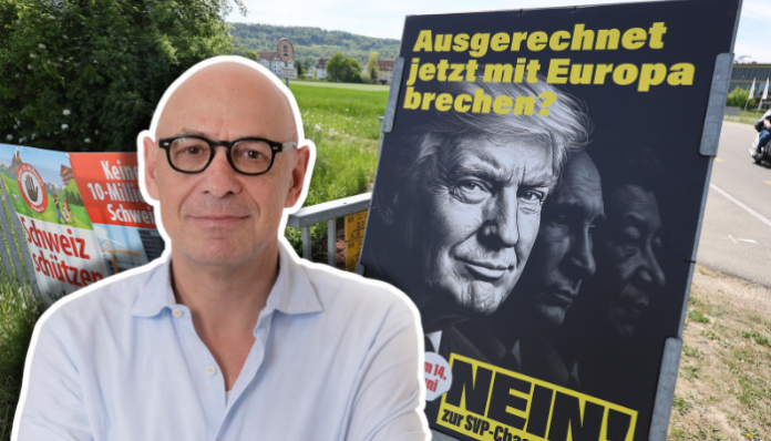 Un homme chauve portant des lunettes noires et une chemise bleu clair se tient devant une affiche politique allemande. L'affiche, sur fond noir, porte le texte en jaune "Ausgerechnet jetzt mit Europa brechen?" (Rompre avec l'Europe maintenant?) et affiche le mot "NEIN!" (NON!) en bas. En arrière-plan, on aperçoit un paysage rural avec des collines verdoyantes, des bâtiments et une route. D'autres affiches électorales sont visibles sur la gauche.