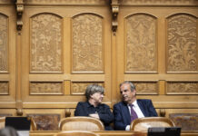 Voici les parlementaires du Centre qui rejettent le gel du salaire minimum Deux personnes en tenue formelle sont assises côte à côte dans un cadre officiel. Elles sont positionnées devant un mur orné de boiseries dorées richement décorées, caractérisé par des panneaux sculptés présentant des motifs floraux et figuratifs élaborés. Les chaises sur lesquelles elles sont assises sont de style classique avec dossiers en rotin. La femme à gauche, vêtue d'une veste noire, regarde vers la droite, tandis que l'homme à droite, portant un costume bleu marine avec une cravate, se tourne légèrement vers elle. L'arrière-plan somptueux suggère un lieu prestigieux tel qu'une institution gouvernementale, un tribunal ou une organisation importante.
