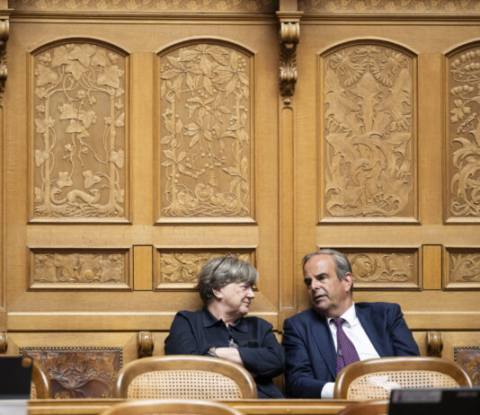 Voici les parlementaires du Centre qui rejettent le gel du salaire minimum Deux personnes en tenue formelle sont assises côte à côte dans un cadre officiel. Elles sont positionnées devant un mur orné de boiseries dorées richement décorées, caractérisé par des panneaux sculptés présentant des motifs floraux et figuratifs élaborés. Les chaises sur lesquelles elles sont assises sont de style classique avec dossiers en rotin. La femme à gauche, vêtue d'une veste noire, regarde vers la droite, tandis que l'homme à droite, portant un costume bleu marine avec une cravate, se tourne légèrement vers elle. L'arrière-plan somptueux suggère un lieu prestigieux tel qu'une institution gouvernementale, un tribunal ou une organisation importante.