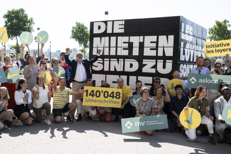 Manifestation de soutien aux locataires en Suisse. Une foule de manifestants se rassemble devant une grande pancarte noire portant le texte "DIE MIETEN SIND ZU HOCH" (Les loyers sont trop élevés). Au centre, un panneau jaune indique "140'048 Unterschriften" (140 048 signatures). Les participants, dont certains tiennent des symboles jaunes et bleus, posent ensemble pour montrer leur mobilisation contre la crise du logement. Des bannières des organisations "Initiative les loyer" et "asloca" sont visibles, témoignant de l'engagement collectif pour des loyers plus abordables.