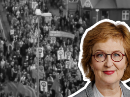 Þórunn Sveinbjarnardóttir : « La grève des femmes nous a montré ce qu’il est possible de faire lorsque les femmes font preuve de solidarité » Portrait d'une femme aux cheveux roux ondulés portant des lunettes rondes et du rouge à lèvres rose, souriant légèrement à la caméra. Elle porte un haut gris. Son portrait est détouré et superposé sur une photographie en noir et blanc historique montrant une foule dense de manifestants tenant des pancartes lors d'un rassemblement public dans une rue urbaine en Islande.