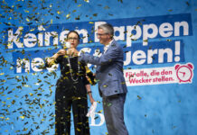 PLR : le prétendu parti de l’économie néglige sa comptabilité Deux personnes en tenues formelles célèbrent devant un grand panneau bleu avec du texte en allemand, tandis que des confettis dorés et noirs tombent autour d'elles. La femme à gauche porte des lunettes et un costume noir, l'homme à droite porte un costume bleu. Le panneau affiche "Keinem oppen" et "nern!" avec un logo rose et le texte "Für alle, die den Wecker stellen."