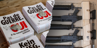 « Pas de guerre » : comment l’UDC trompe l’électorat Collage montrant à gauche des affiches de protestation suisse avec les slogans 'Pas de GUERRE' et 'Kein KRIEG' (Non à la guerre en français et allemand) avec le logo du référendum suisse, et à droite une boîte en bois contenant un arsenal organisé de plusieurs fusils d'assaut noirs alignés horizontalement avec des chargeurs et accessoires tactiques.